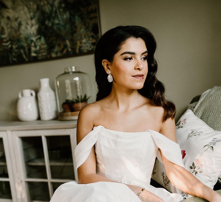 Bride in a structured wedding dress with pearl earrings and her hair styled in Hollywood waves