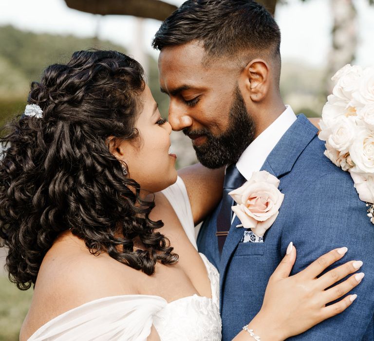 Bride & groom embrace lovingly outdoors as bride wears off the shoulder sheer sleeve sweetheart neckline wedding dress