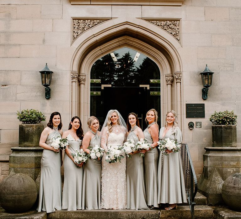 Bride stands with her bridesmaids in satin sage green bridesmaid dresses in different styles 