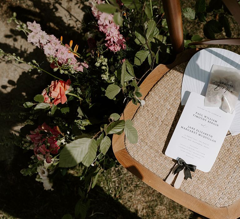 White stationery and fan complete with small bag of confetti on wicker chair outdoors