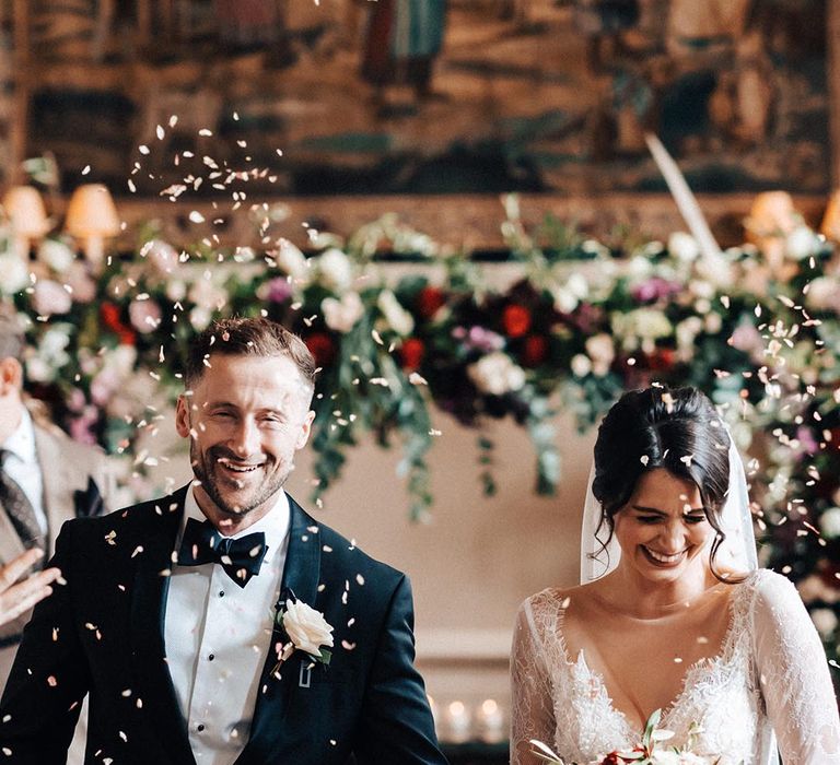 The bride in a traditional lace long sleeve Milla Nova wedding dress walking back down the groom to confetti 