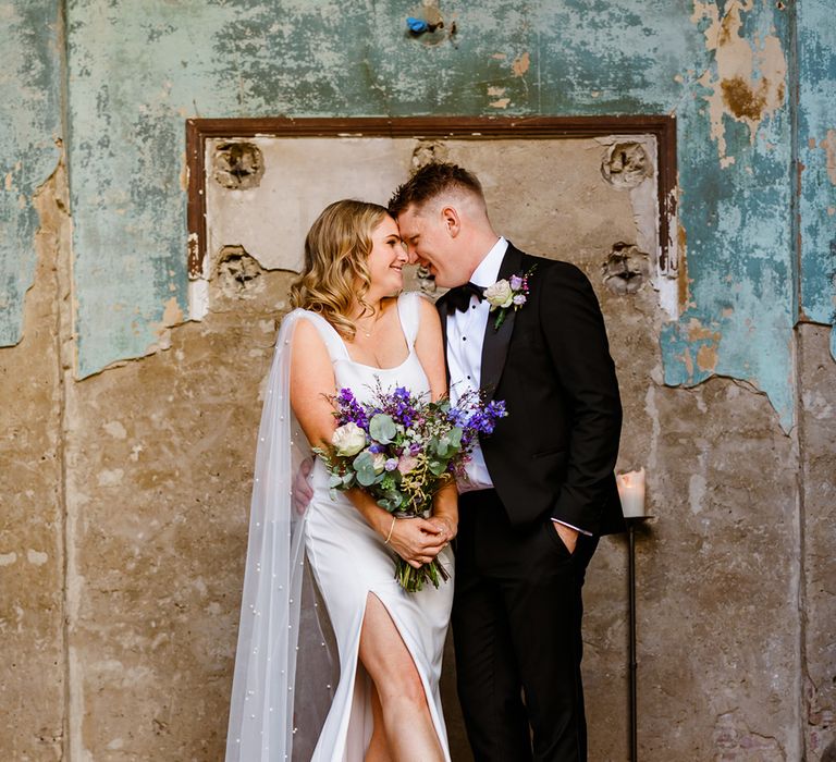 Bride holds colourful bouquet and stands beside her groom in black tie 