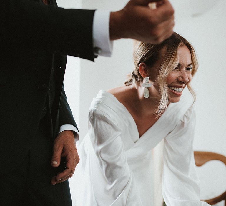 Bride wears statement earrings and bell sleeve wrap silk wedding dress 