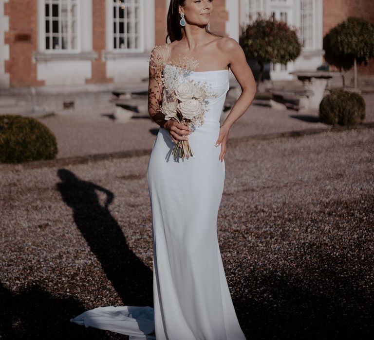 Bride in strapless satin wedding dress with two tier veil and azure blue drop earrings holding bouquet with large white roses and dried flowers 