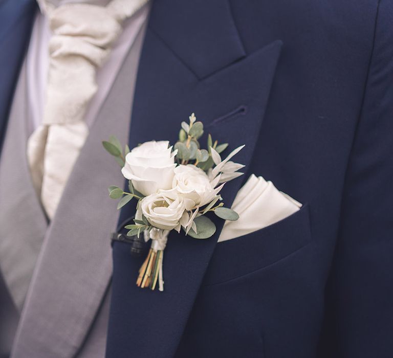 Groom in navy suit with grey waistcoat with a white tie and a white rose buttonhole 