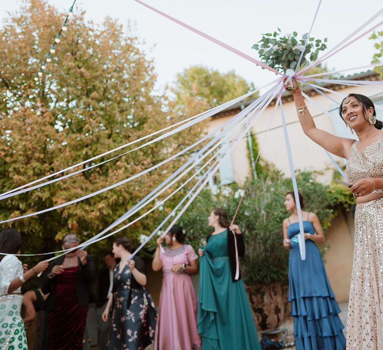 bride in a sparkly gold dress holding up her bouquet with ribbons attached 