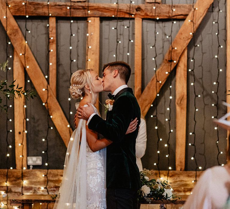 The bride with pearl hair accessories kisses the groom as they share their first kiss as a married couple