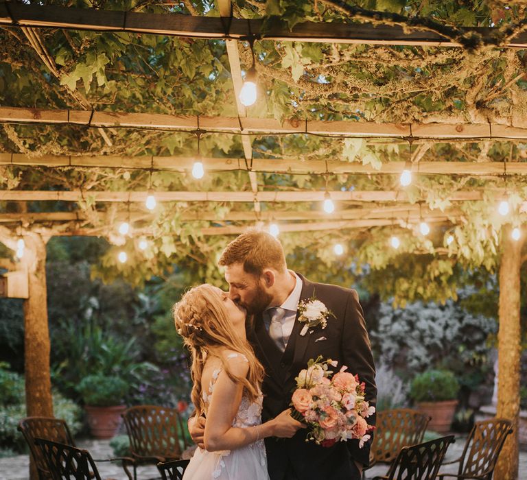 Bride with braided hair wearing an Anna Kara wedding dress kissing the groom for marquee wedding at home in Devon 