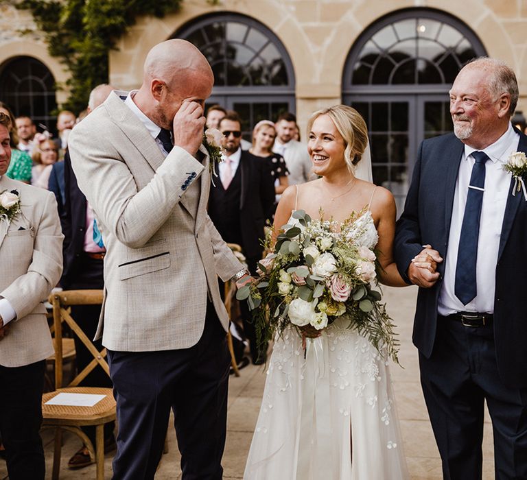 Floral applique wedding dress worn by the bride as she is walked to the end of the aisle by her father to meet the groom 