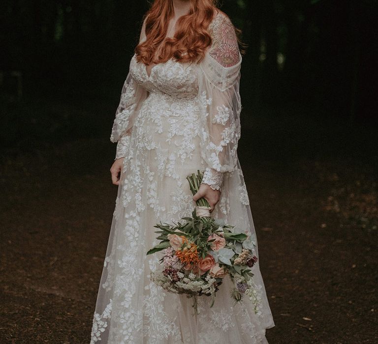 Bride in stunning off the shoulder long sleeve floral lace wedding dress with pink flower crown and matching bridal bouquet 