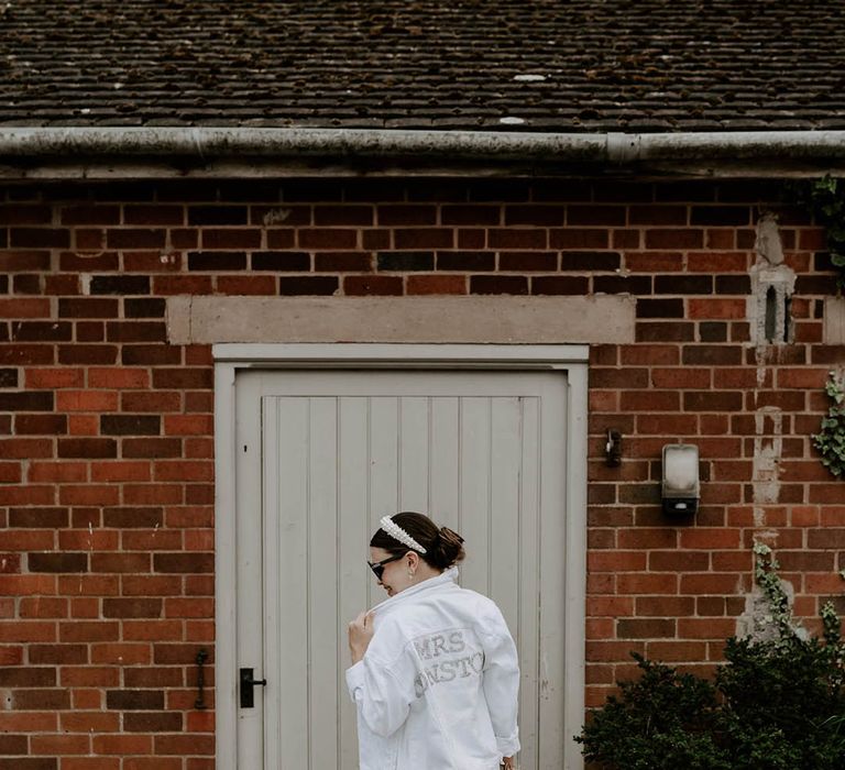 Bride in pearl headband and white denim jacket with personalised pearl name on the back of the jacket with black sunglasses 