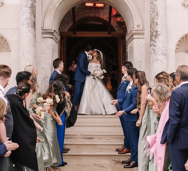 The bride and groom share a romantic kiss as they walk out of Lulworth Castle wedding venue 