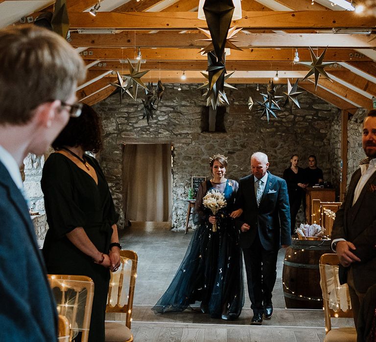 Bride in bespoke navy blue wedding dress with gold stars on being walked down the aisle by her father 