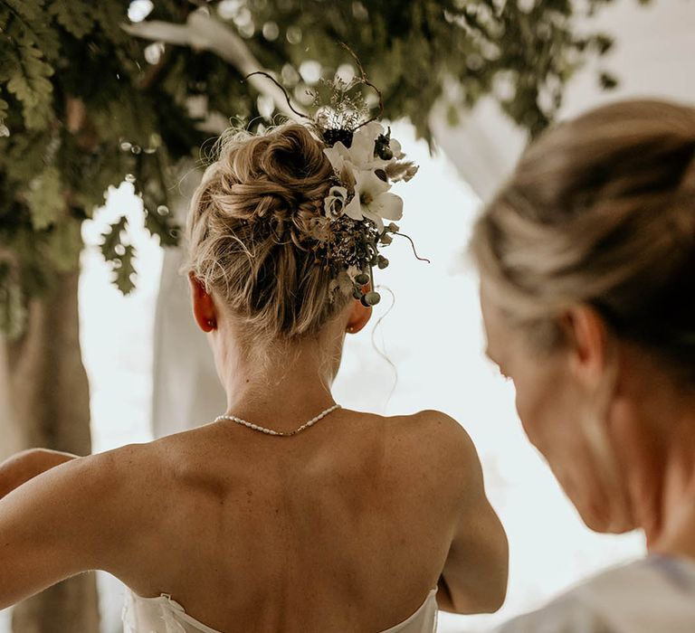 Bride wearing a strapless corset style wedding dress with dainty pearl necklace and updo decorated with flower hair accessories 