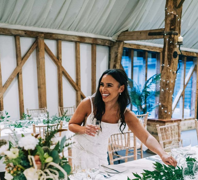 Bride in a-line tulle wedding dress with beaded lace applique with petals and a square neckline with side tulle cutouts standing by rustic wedding tablescape at South Farm wedding with white tablecloth, foliage wedding table runners and pampas grass, eucalyptus, blush garden roses, dried flowers and foliage floral centrepieces 