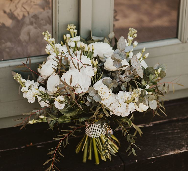 Classic and traditional white wedding bouquet with roses and eucalyptus tied together with diamantés