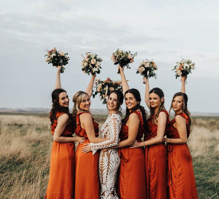 Bridesmaids in ruffle orange bridesmaid dresses with the bride in a long sleeve boho lace wedding dress 