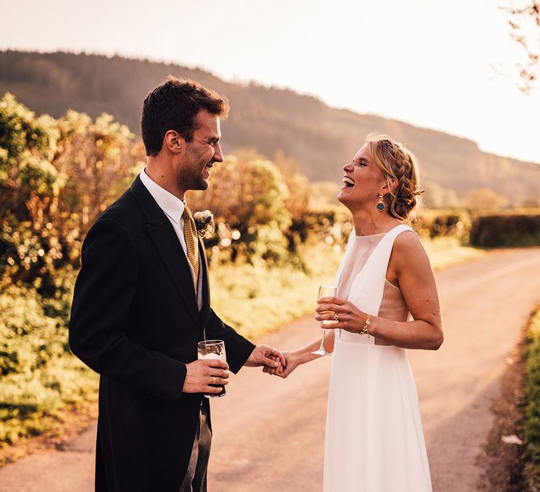 The bride wearing a classic white wedding dress with blue and gold earrings smiling with the groom 