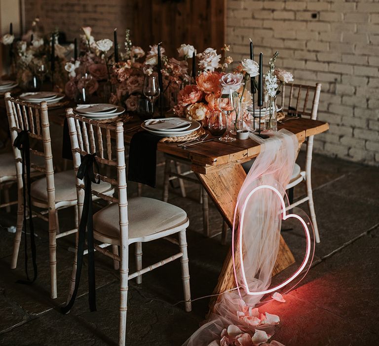 Huge hanging fringe garland installation over wedding table with pink heart neon sign with black chair ribbons and accent candles 