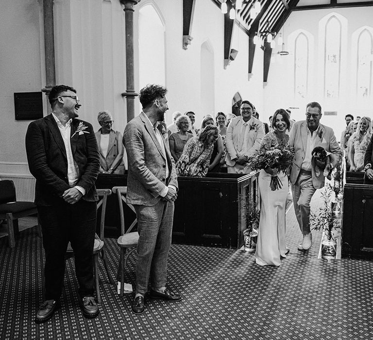 Traditional church wedding ceremony with the bride and father of the bride walking down the aisle with a pet dog ring bearer 