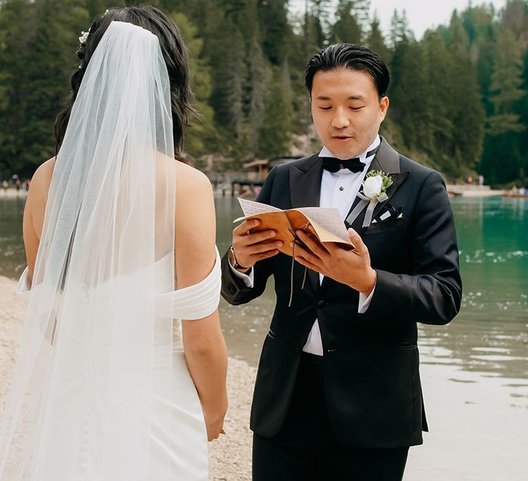 The groom in a black tuxedo reads out his personalised wedding vows from the booklet 