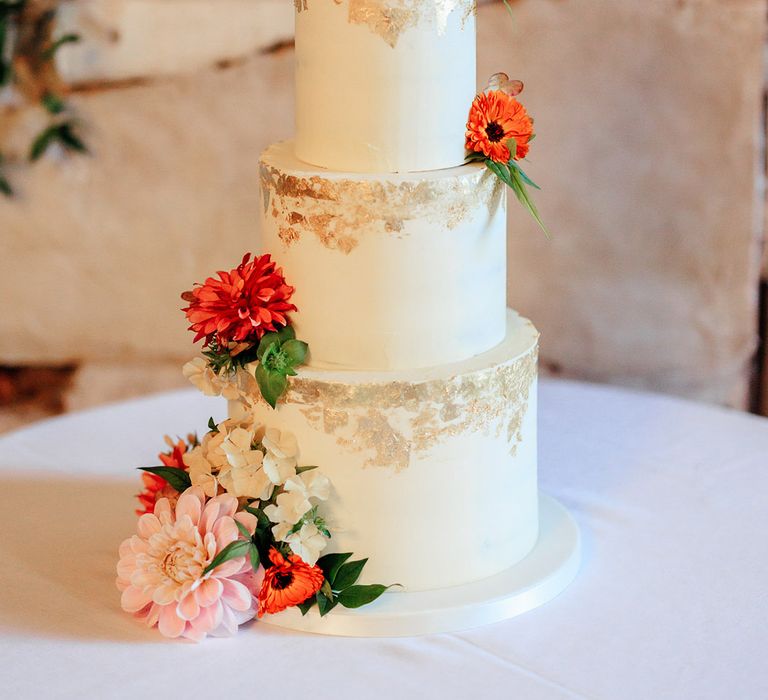 Three tier white iced wedding cake with gold flakes with pink flower decorations 