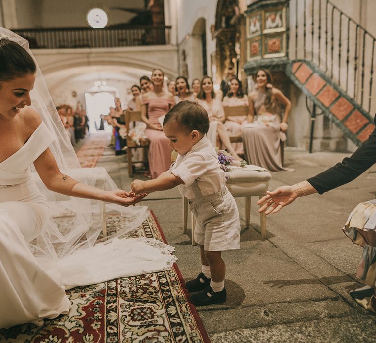 Page boy in shorts and braces giving the bride the rings at the church wedding ceremony 