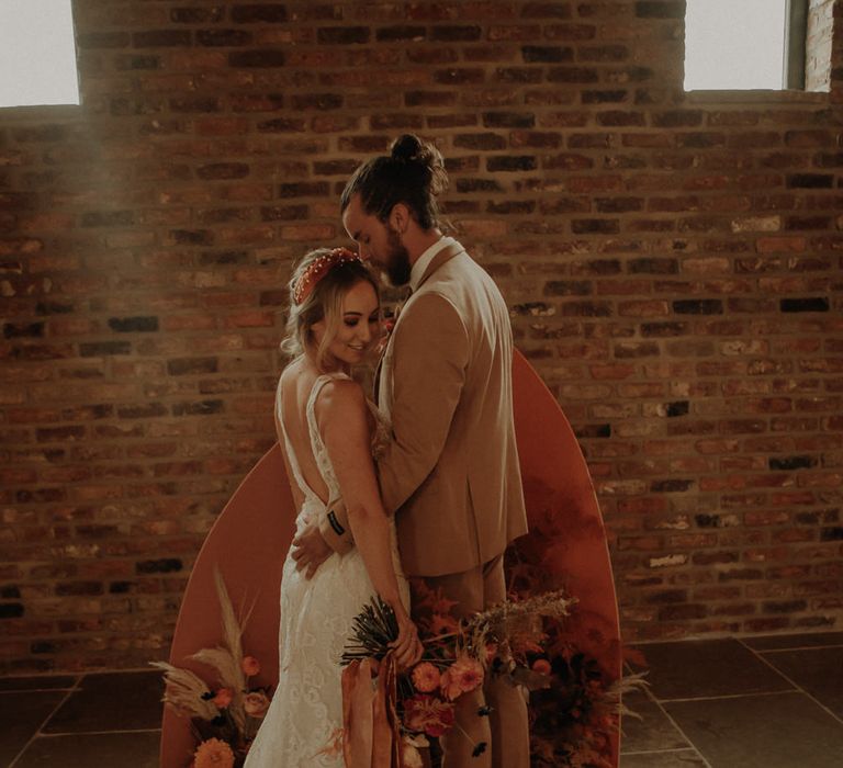 Bride and groom standing in front of an orange board and floral altar