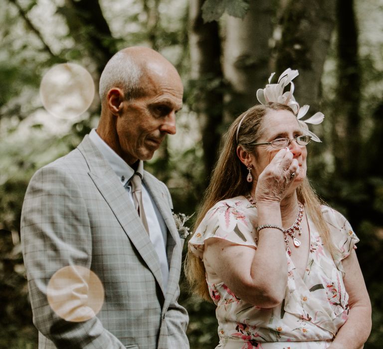 Wedding guests shed a tear at the ceremony in a light grey suit and ruffle floral wrap dress