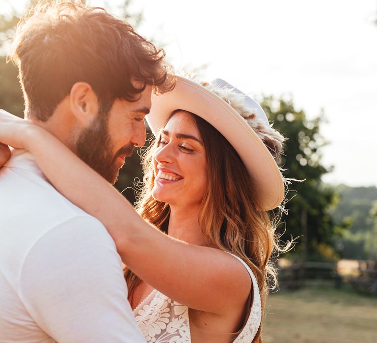 Bride embraces groom whilst wearing a white bridal fedora