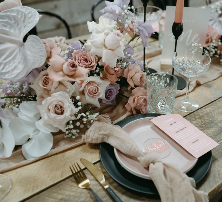 Place setting with pink and purple tableware, napkin, menu card and wedding flowers 