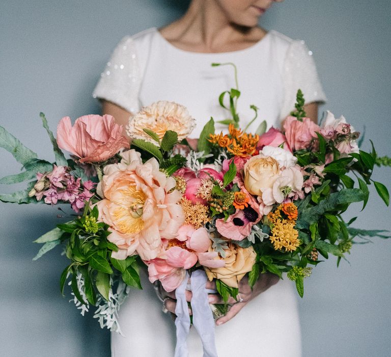 Bride holding pink, orange and white anemone and rose wedding bouquet 