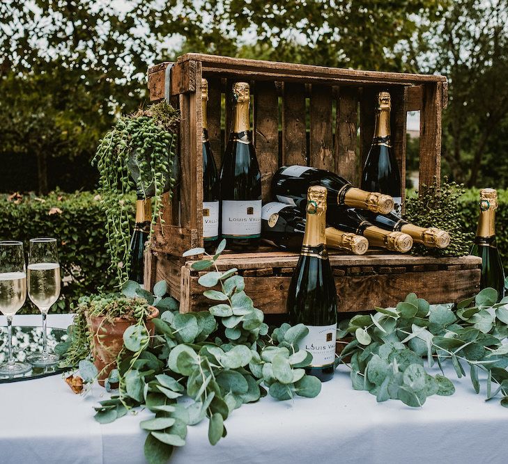 Rustic crates display bottles of champagne. Champagne flutes are lined up next to the crates and filled with champagne.