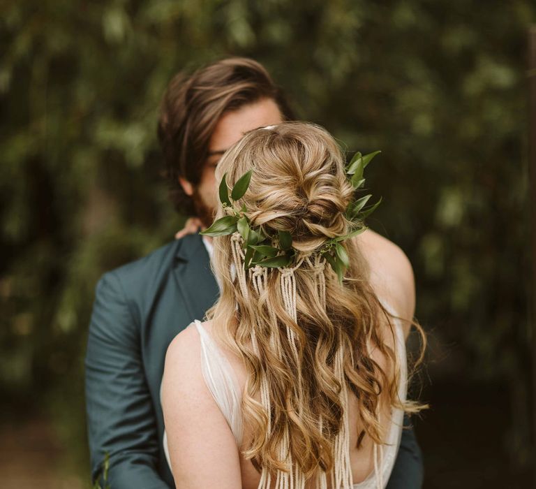 Bride wears her hair in loose curls featuring green foliage and Macrame headware