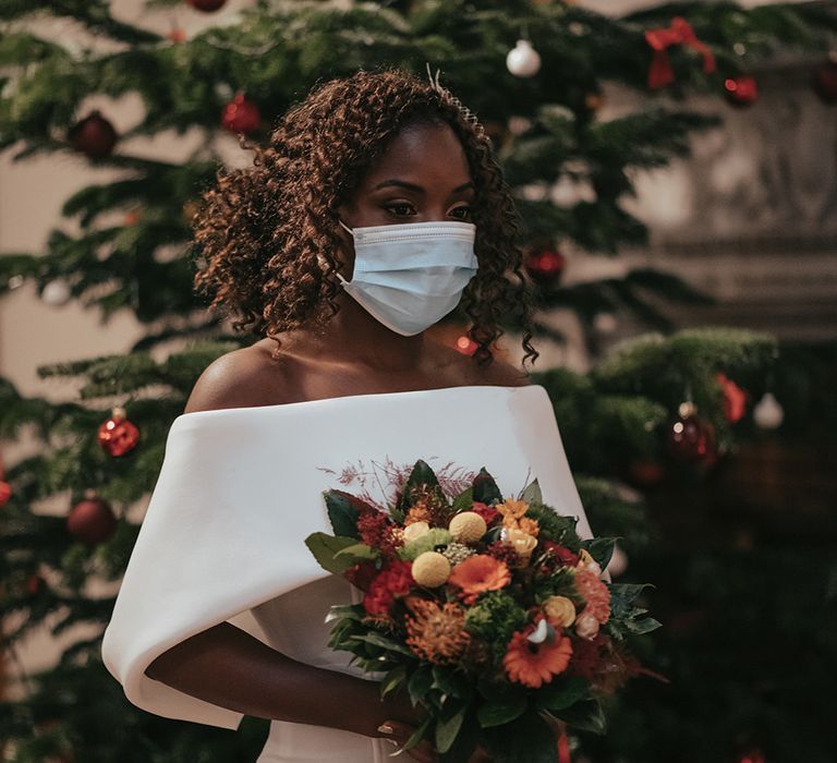 Bride carries Autumnal bouquet whilst wearing a mask