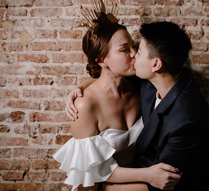 Asian Lesbian wedding with bride in a strapless wedding dress and celestial headdress kissing her partner in a navy suit jacket 