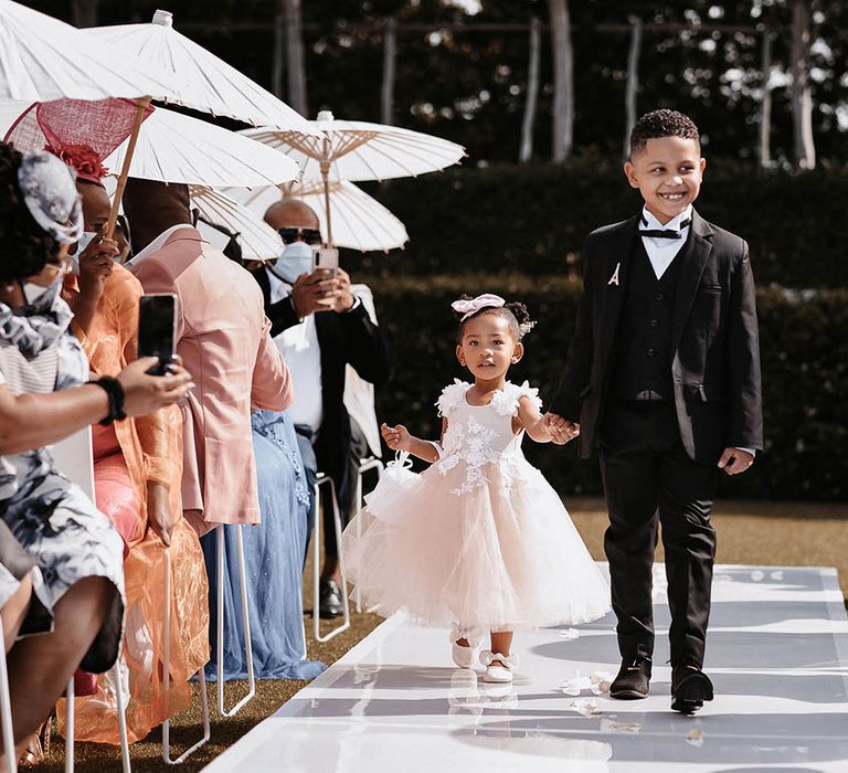 Page boy in miniature tuxedo and flower girl in a pink tulle dress walking down the aisle 