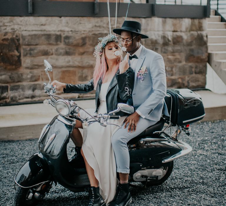 Alternative bride and groom sitting on a Motorbike with pastel pink, blue and black balloons tied to the back