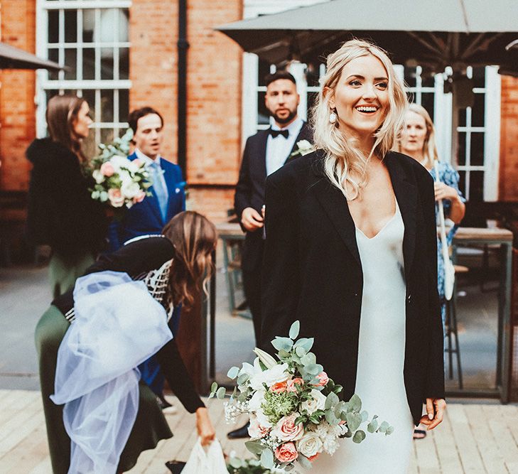 Bride in a Dove Grace Loves Lace wedding dress with black jacket holding her peach and green bouquet 