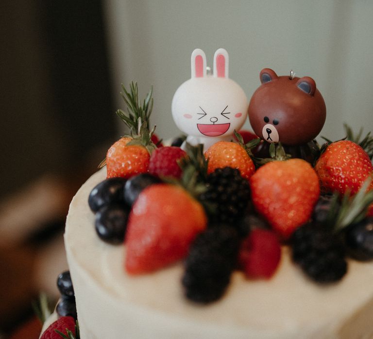 Cute cartoon animal cake toppers on a white wedding cake with mixed berries