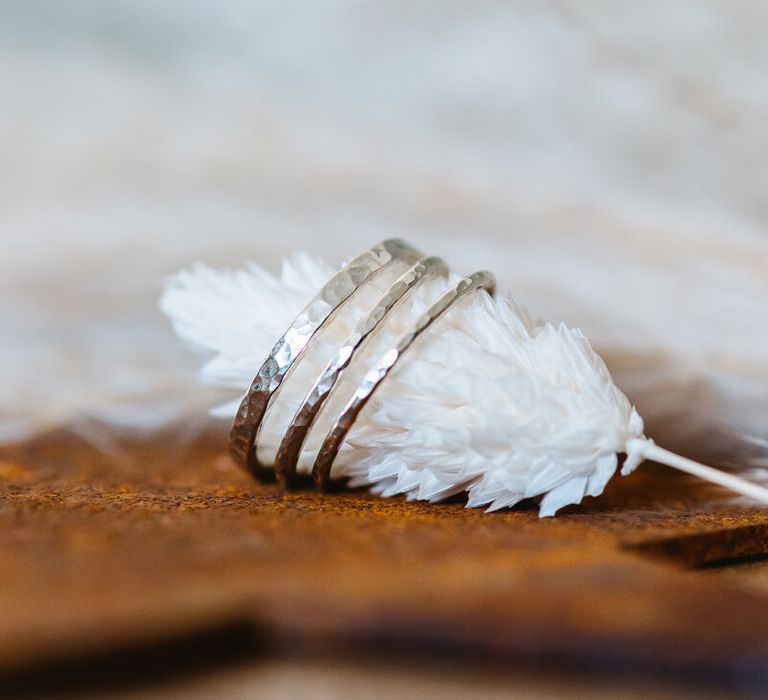 Three stacked silver wedding rings by Nikki Stark around a piece of pampas grass