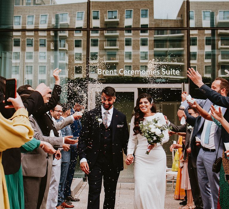 Confetti moment with bride in a fitted wedding dress with long sleeves and groom in a navy suit with floral tie 