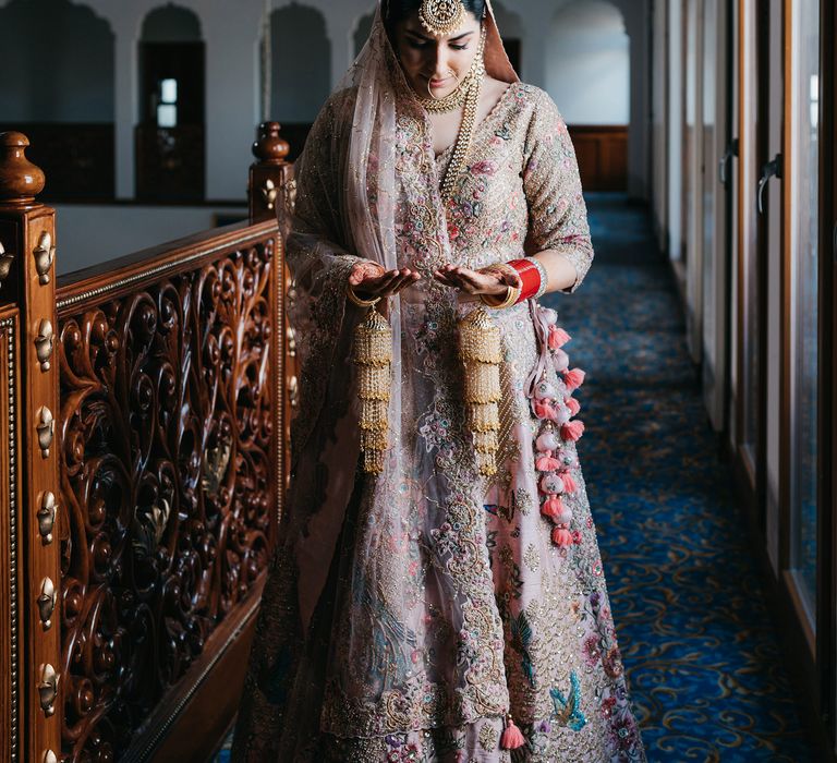 Bride wears bespoke Lehengha and looks at her palms covered with traditional Henna