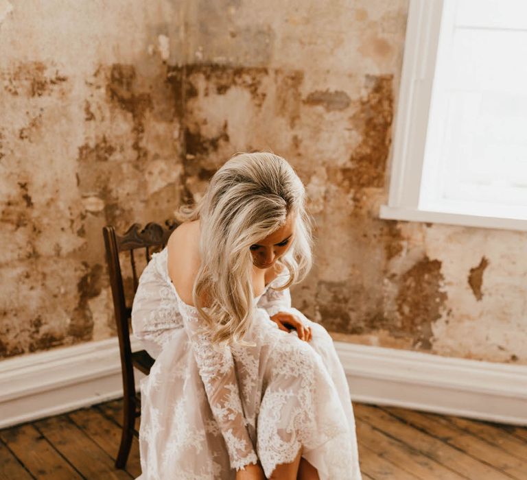 Bride sitting in a chair in an empty industrial style room, fixing her fluffy white bridal heels