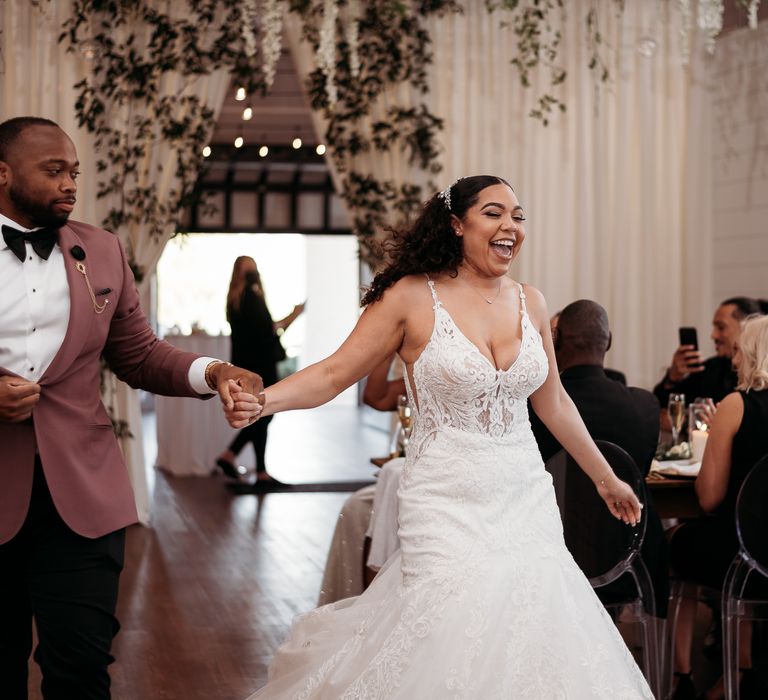 Bride & groom laugh and hold hands as they walk through wedding reception venue with one another