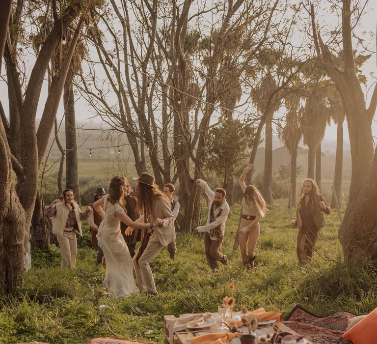 Bride & groom dance with their wedding party in the woodland as they sun shines through the trees