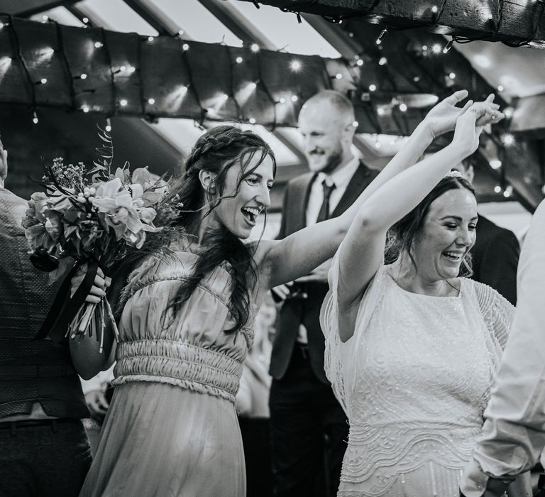 Bride dances with her bridesmaid on the day of her wedding as they laugh together