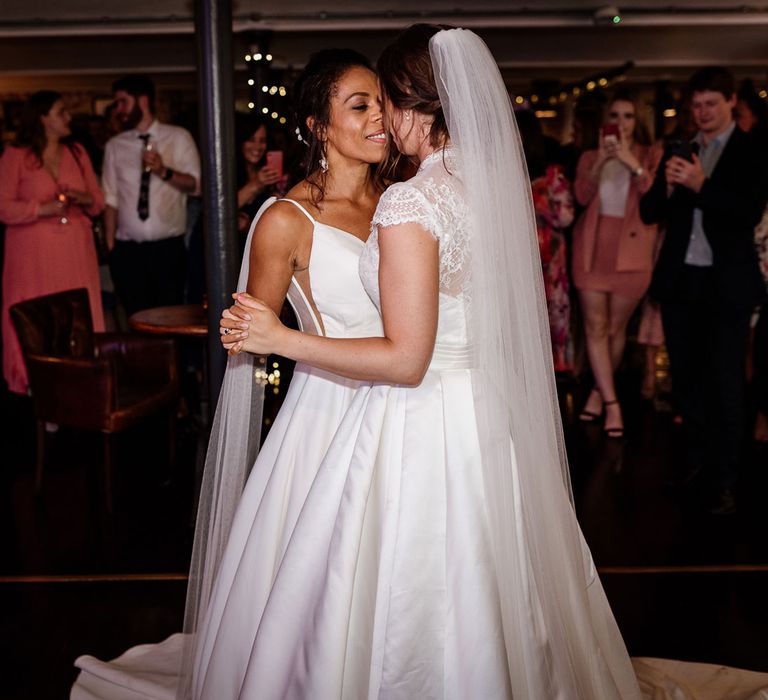 Bride in white cami wedding dress with shoulder veil details dances with bride in white lace top capped sleeve wedding dress an veil during wedding reception at The West Mill Derby