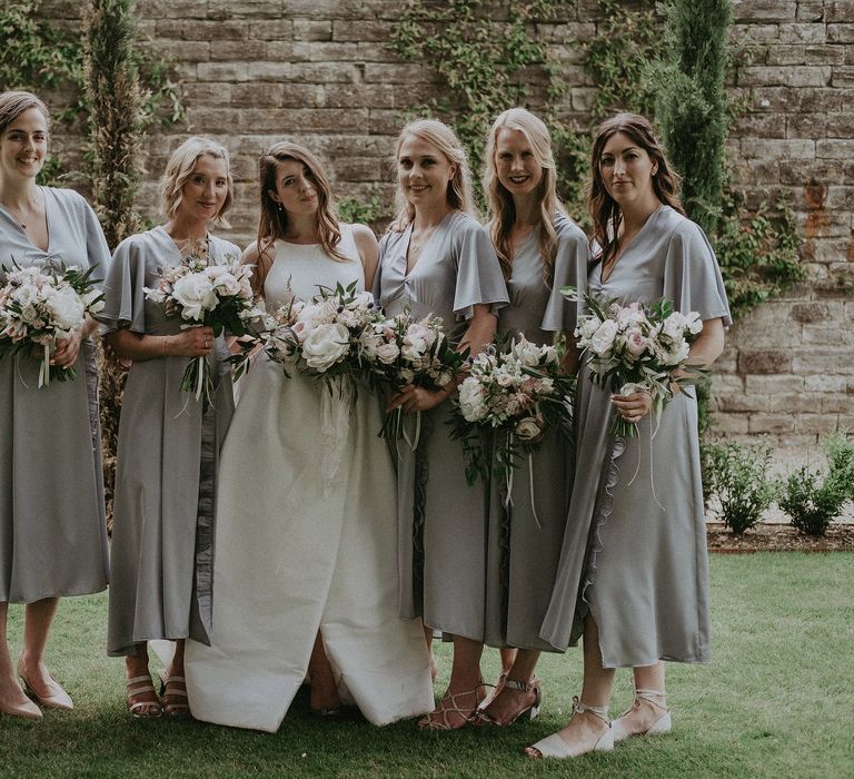 Bride stands with her bridesmaids who wear handmade dresses with batwing sleeves and split front skirt