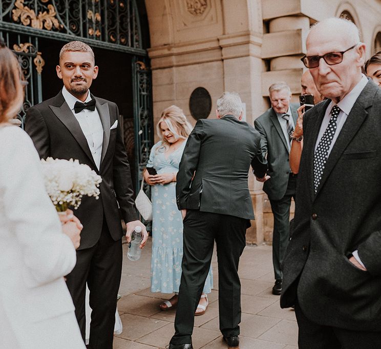 Groom in a tuxedo and wedding guests gathered outside Sheffield Registry Office 